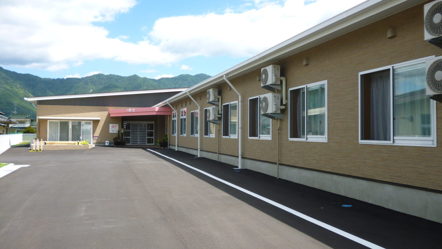 山々を背景とした介護施設の建物外観。駐車場から見た正面玄関周辺。